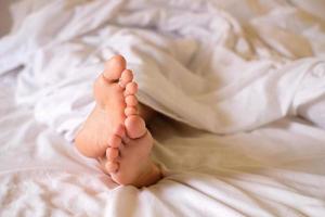 deux pieds de femme éveillée sur un matelas et une couverture blanche, photo du matin, concept de soins de santé