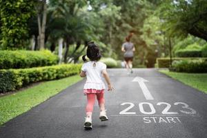 bébé asiatique en cours d'exécution commence dans la nouvelle année 2023. démarrage d'une femme coureuse qui court sur une piste de course nature aller à l'objectif de réussite. personnes courant dans le cadre du numéro 2023. soins de santé sportifs. photo