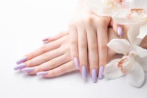 les mains de la fille avec une délicate manucure violette et des fleurs d'orchidées photo