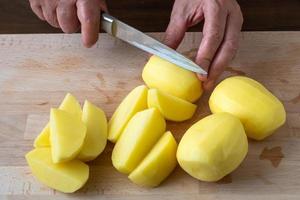 mains avec couteau coupant les pommes de terre, préparant les pommes de terre pour la cuisson. photo