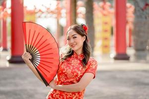 joyeux festival du nouvel an chinois lunaire. belle femme asiatique portant un costume traditionnel de cheongsam qipao tenant un ventilateur dans un temple bouddhiste chinois. photo