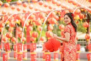 femme asiatique heureuse vêtue d'une robe traditionnelle cheongsam qipao tenant une lanterne tout en visitant le temple bouddhiste chinois. célébrer le nouvel an lunaire chinois, les vacances de la saison des fêtes. émotion sourire photo