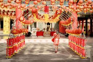 jeune femme asiatique vêtue d'une robe traditionnelle cheongsam qipao tenant une lanterne et marchant avec son dos tout en visitant le temple bouddhiste chinois. célébrer le nouvel an lunaire chinois. photo