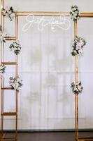 conception d'arche rectangulaire en métal doré de mariage avec des fleurs blanches fraîches et des verts sur un fond de mur blanc. décoration festive zone photo à l'intérieur