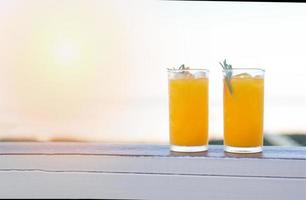 verre de jus d'orange sur une table en bois, jus d'orange frais avec des fruits orange et du romarin le matin voir le fond de la nature photo