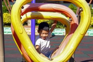 garçon asiatique heureux et aime grimper sur des cerceaux en plastique dans l'aire de jeux. mise au point douce et sélective. photo