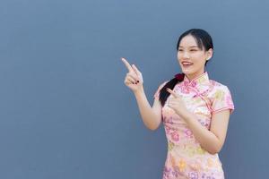 belle femme asiatique aux cheveux longs qui porte une robe cheongsam rose sur le thème du nouvel an chinois tandis que sa main montre pour présenter quelque chose et montre la main pour pointer et regarde la caméra. photo