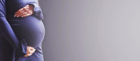 gros plan du ventre de la femme enceinte. mains étreignant le ventre sur fond bleu. concept de santé maternelle photo