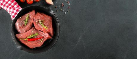 viande crue. steak de boeuf cru sur un tableau noir avec des herbes et des épices. vue de dessus. bannière pour la conception photo