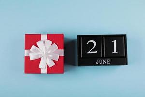 coffret cadeau rouge et calendrier en bois noir date 21 juin sur fond bleu. notion de fête des pères. mise à plat, vue de dessus photo