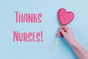 carte de remerciement des infirmières. main tenant un coeur rose. vacances, concept de carte de voeux. fond pastel bleu