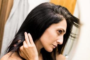portrait d'une belle jeune femme examinant son cuir chevelu et ses cheveux devant le miroir, les racines des cheveux, la couleur, les cheveux gris, la perte de cheveux ou le problème du cuir chevelu sec photo