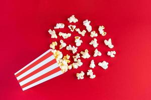 Pop-corn au fromage savoureux tombant d'un seau en carton à rayures rouges, isolé sur fond rouge photo