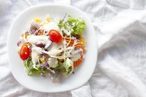 vue de dessus d'une salade de légumes et de fruits mélangés dans une assiette blanche sur une nappe blanche.