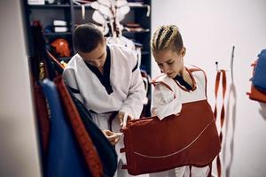 une combattante de taekwondo handicapée habille une armure de poitrine avec l'aide de son entraîneur dans le vestiaire. photo