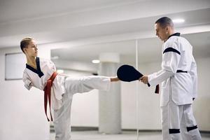 femme athlétique motivée avec un handicap pratiquant le coup de jambe avec un entraîneur de taekwondo dans un club de santé. photo