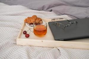 un plateau avec un ordinateur portable et une tasse de thé sur le lit dans la chambre.travail à domicile, apprentissage à distance ou passe-temps confortable en ligne. photo