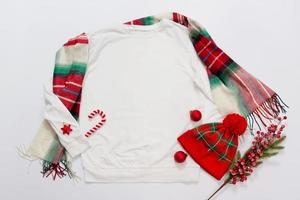 gros plan sur l'espace de copie de sweat-shirt modèle vierge blanc. concept de vacances de noël. sweat-shirt maquette vue de dessus, chapeau. décorations de fêtes rouges sur fond blanc. accessoires de bonne année. tenue de Noël photo