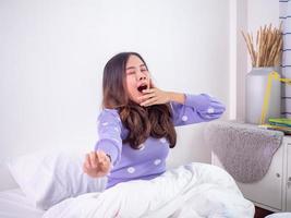 la fille se réveille le matin allongée sur le lit, toujours somnolente, se tordant et bâillant dans la chambre. femme paresseuse le week-end photo