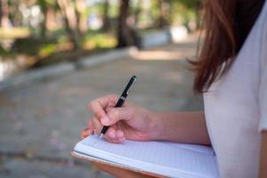 femme assise écrivant un dossier dans un petit livre dans le jardin confortablement. photo