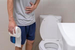 diarrhée, douleurs abdominales, concept de constipation. les hommes ont des contractions et des douleurs à l'estomac. homme tenant du papier toilette dans les toilettes. photo