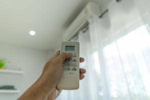 la main de l'homme sur le climatiseur en tenant la télécommande sur le système de refroidissement après que personne ne soit dans la pièce. économiser de l'électricité, économiser de l'énergie et protéger l'environnement. photo