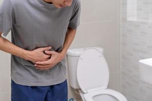 l'homme debout a la diarrhée et des aliments très toxiques. l'homme touche le ventre dans la salle de bain. douleur abdominale, diarrhée, concept de cancer du côlon photo