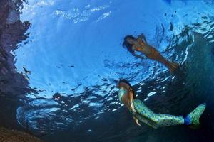 deux sirènes nageant sous l'eau dans la mer d'un bleu profond photo