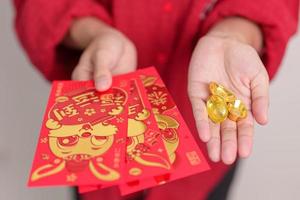 femme tenant une enveloppe rouge chinoise avec des lingots d'or, cadeau d'argent pour les vacances de bonne année lunaire. phrase chinoise signifie bonheur, en bonne santé, chanceux et riche photo