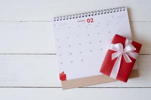 boîte-cadeau rouge sur calendrier isolé sur fond en bois blanc avec. notion de saint valentin. planification agenda, événement, organisateur saint valentin. mise à plat, vue de dessus. photo