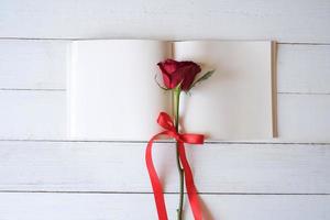 cahier vierge avec des roses rouges sur une table en bois. copiez l'espace pour votre texte. concept de la saint-valentin, mariage, anniversaire et occasion spéciale. copier l'espace pour le texte. vue de dessus, mise à plat. photo