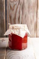 bocal en verre fermé de confiture de fraises maison est debout sur une table en bois. photo