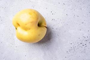 une pomme jaune laide sur fond de béton gris. photo