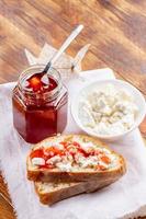 sandwich au caillé et confiture de fraises, pot de confiture de fraises et bol de caillé sur une serviette blanche sur une table en bois. photo