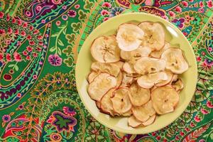 assiette verte ronde avec des chips de pomme saines sur un tissu floral vert vif. photo