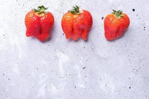 trois fraises rouges laides sur fond de béton gris. photo