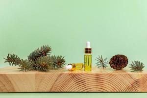 composition avec de l'huile essentielle d'épinette dans de petites bouteilles en verre, brindilles, cône sur support en bois sur fond vert clair. photo