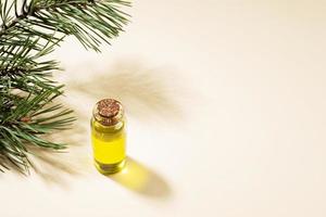 petite bouteille en verre d'huile essentielle de pin avec branche de pin et ombres sur fond beige. photo