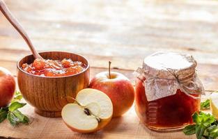 bol en bois et bocal en verre avec confiture de pomme et pommes et menthe verte sur fond en bois. photo