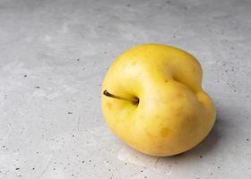 une pomme jaune laide avec dent sur fond de béton gris. photo