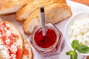 petit-déjeuner sain fait maison avec du pain, de la confiture de fraises sucrées et du lait caillé sur une serviette blanche. photo