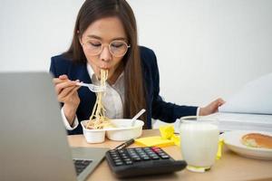 femme d'affaires occupée et fatiguée mangeant des spaghettis pour le déjeuner au bureau et travaillant pour fournir des états financiers à un patron. surmené et malsain pour les plats préparés, concept d'épuisement professionnel. photo