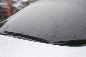 goutte de bruine de pluie sur le pare-brise en verre le soir. arrêter la rue de la voiture sous la pluie battante en ville. Veuillez conduire la voiture avec prudence, route glissante. mise au point douce. photo