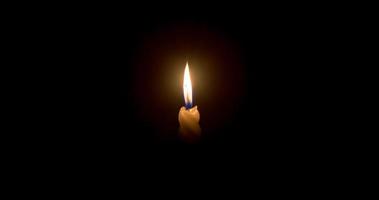 une seule flamme de bougie allumée ou une lumière rougeoyante sur une bougie blanche en spirale sur fond noir ou sombre sur une table à l'église pour noël, des funérailles ou un service commémoratif photo