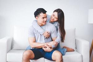 les jeunes couples asiatiques s'embrassent joyeusement sur le canapé du salon à la maison. le concept de création d'une famille de couples mariés photo
