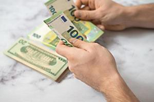 un homme compte des dollars et des euros avec ses mains sur un fond clair photo