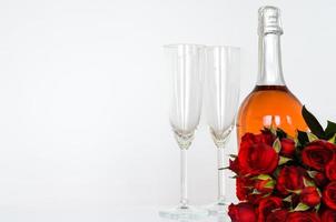 Deux verres vides avec une bouteille de vin rosé pétillant sur fond blanc avec des roses rouges floues pour le concept de restauration de la Saint-Valentin. photo