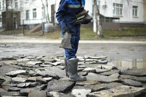 le travailleur jette des pierres sur la route. mauvais état des routes. le constructeur choisit les débris de construction. photo