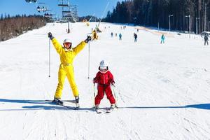 mère et fille s'amusant et apprenant à skier en faisant leurs premiers pas avec le soutien de maman dans une station de ski d'hiver à Mountain Hill. photo