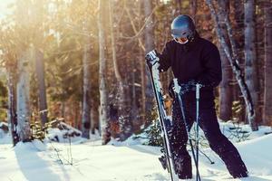 skieur prêt à tenir du matériel de ski avec rétro-éclairage solaire sur la piste de ski - jeune athlète dans les montagnes enneigées pour les vacances d'hiver - concept de sport et concept de vacances - se concentrer sur son visage - filtre chaud photo